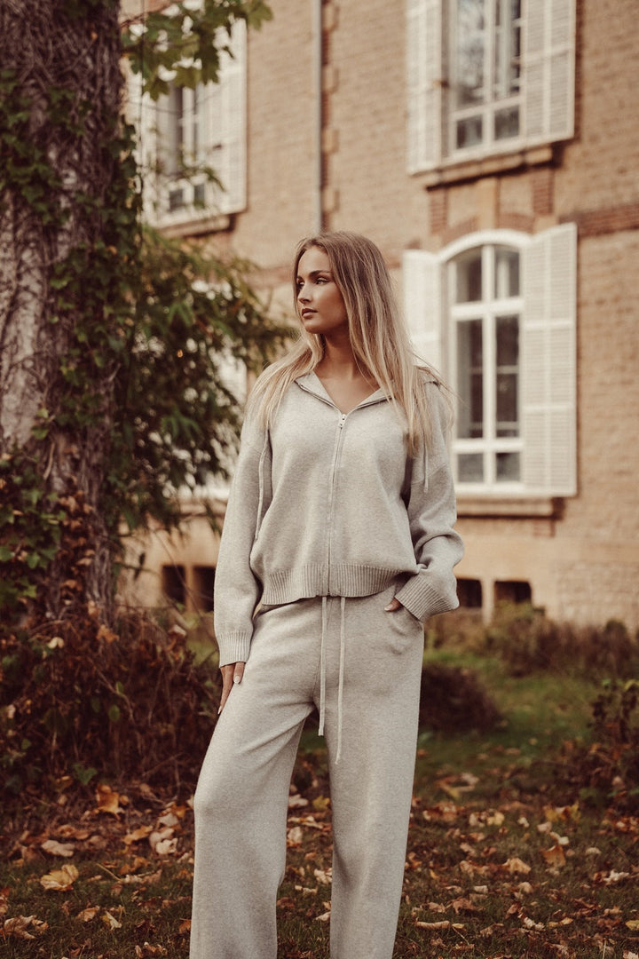 Grey knitted lounge set with zip-up hoodie and wide-leg trousers, worn outdoors in an autumn garden