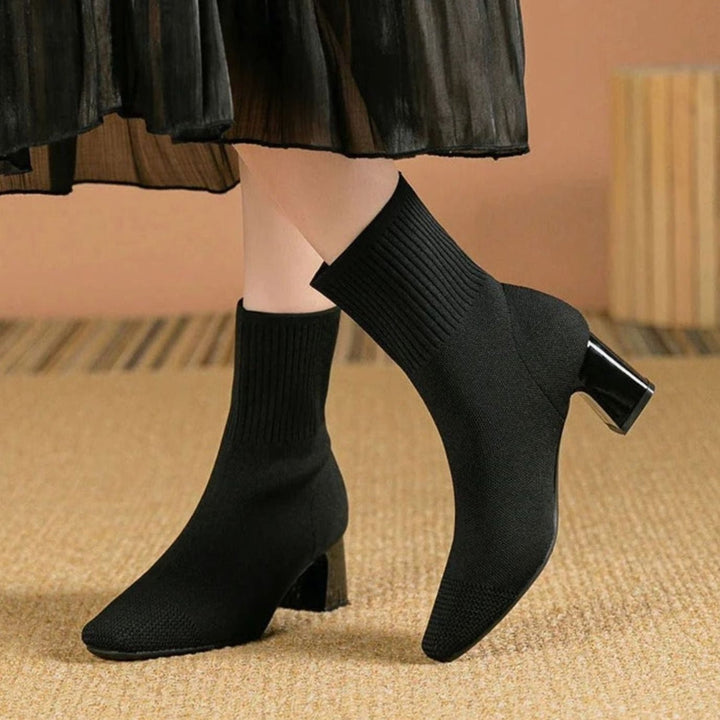 Black rib-knit sock boots with block heel, worn with a pleated skirt