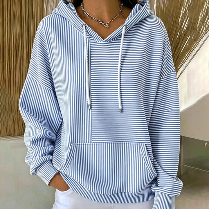 Woman wearing a light blue striped hoodie with white drawcords and a kangaroo pocket, with white trousers | Grace Aura