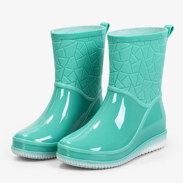 A pair of glossy mint green mid-calf slip-on rain boots with an embossed geometric pattern on the shaft, rear pull tabs and translucent white soles, shown at a three quarter angle on a plain light grey background.
