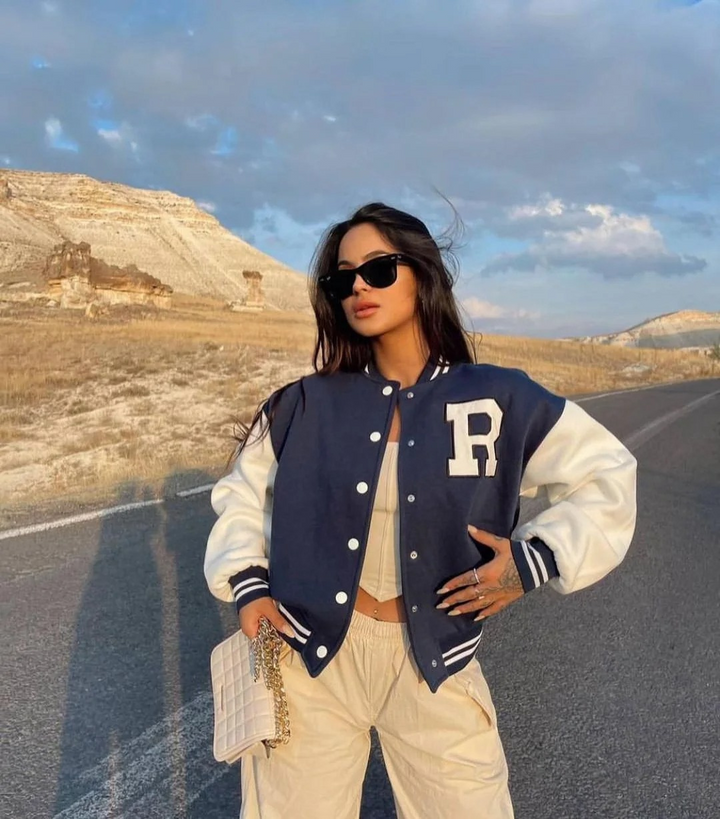 Woman wearing navy and white varsity bomber jacket with cream trousers outdoors | Grace Aura