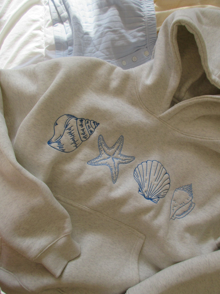 Beige hoodie with embroidered seashell and starfish design, laid flat | Grace Aura