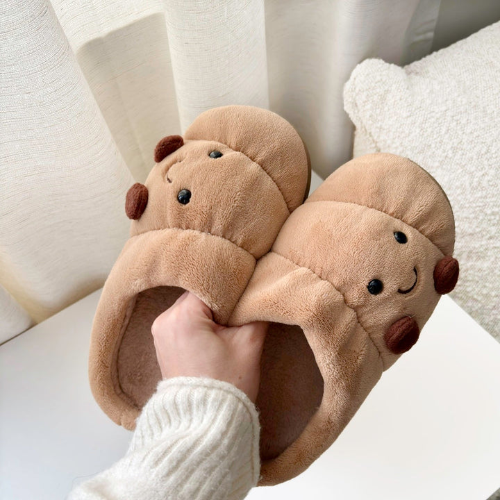 Hand holding tan plush croissant slippers with smiling face embroidery | Grace Aura