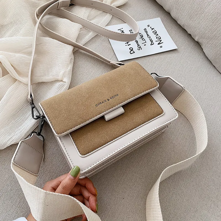 Beige suede and leather crossbody bag with wide strap, held by hand | Grace Aura