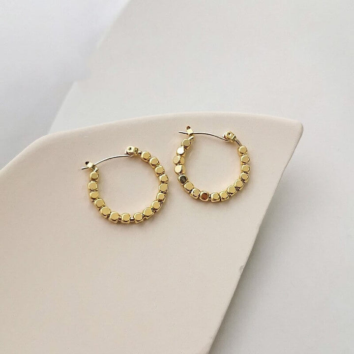 Gold cube bead hoop earrings displayed flat on beige surface | Grace Aura