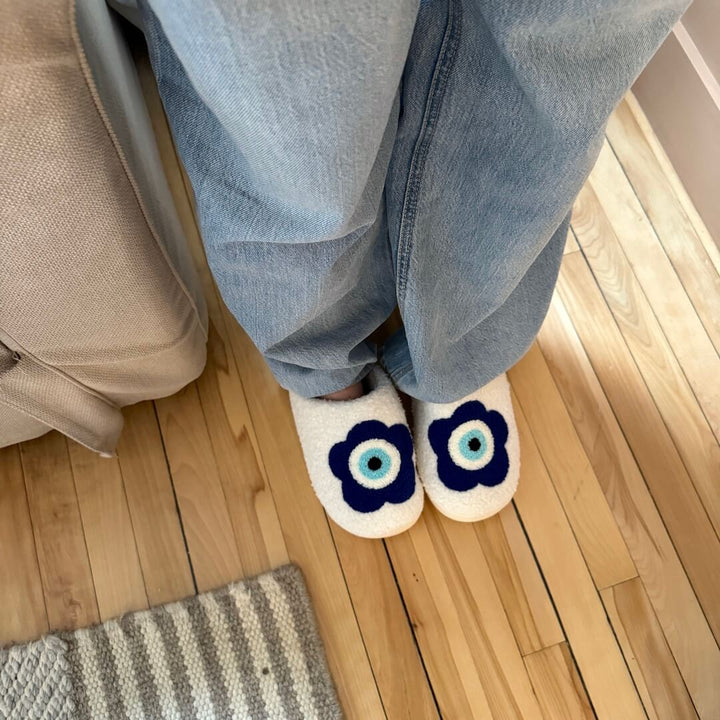 Cream plush slippers with navy flower print, worn on feet, wood floor | Grace Aura