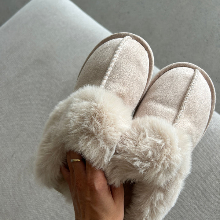 Beige suede slippers with fluffy faux fur trim held by hand | Grace Aura