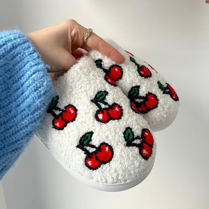 White fuzzy slippers with red cherry print, held by hand | Grace Aura