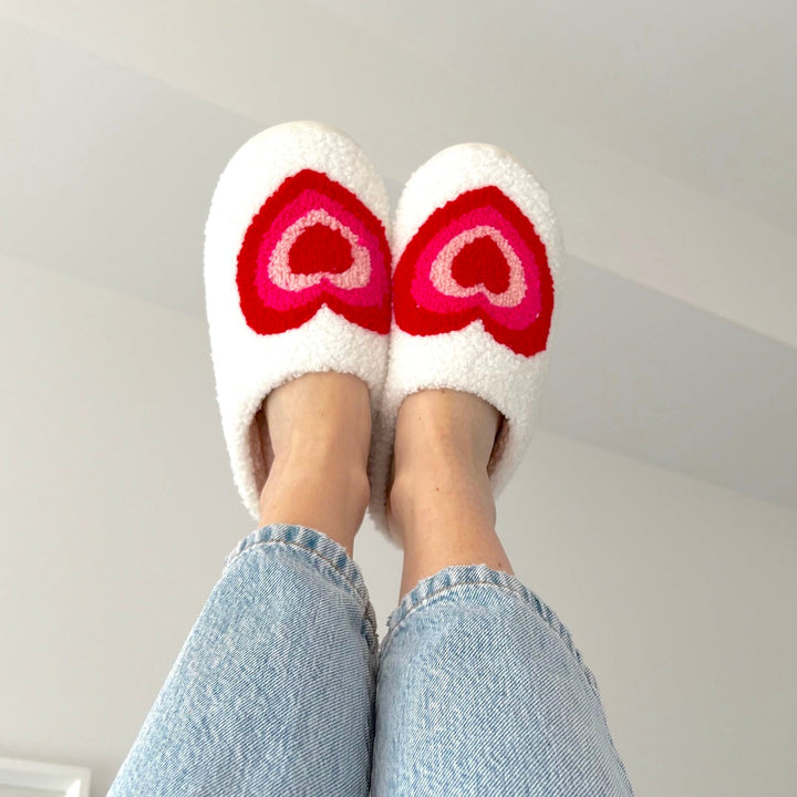 White plush slippers with pink and red heart pattern, worn by person | Grace Aura