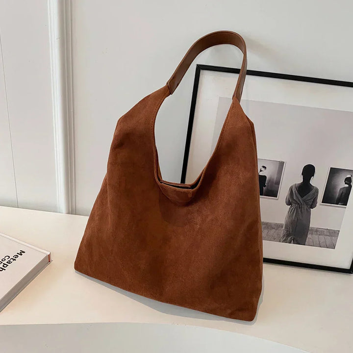 Brown suede hobo tote bag standing upright on white table surface | Grace Aura