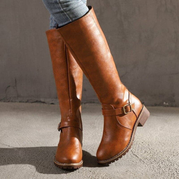 Brown leather knee-high boots with ankle strap buckle, worn by model | Grace Aura