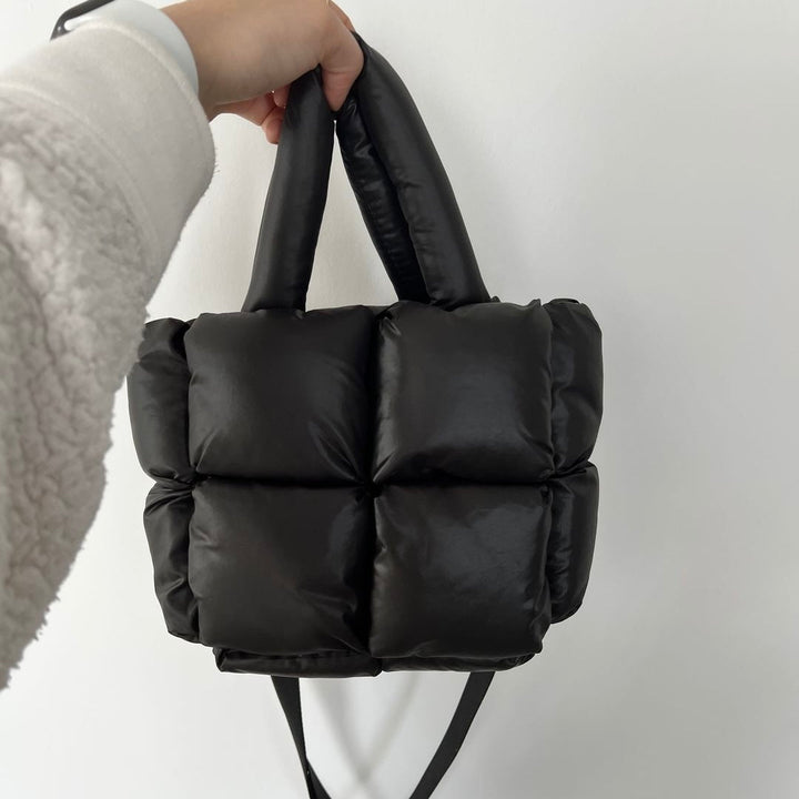 Black quilted puffer tote bag with padded handle, held by hand | Grace Aura
