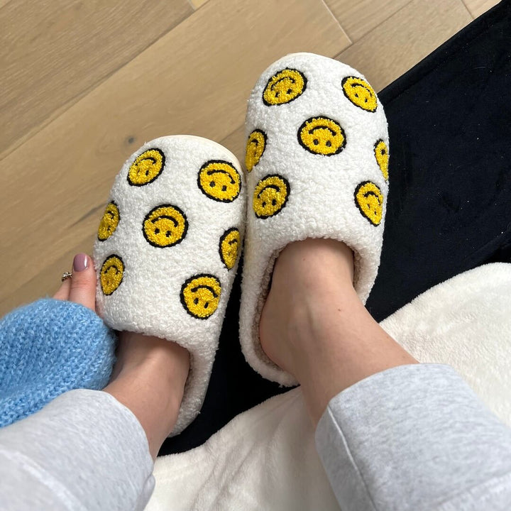 White fuzzy slippers with yellow smiley faces, worn by person standing | Grace Aura