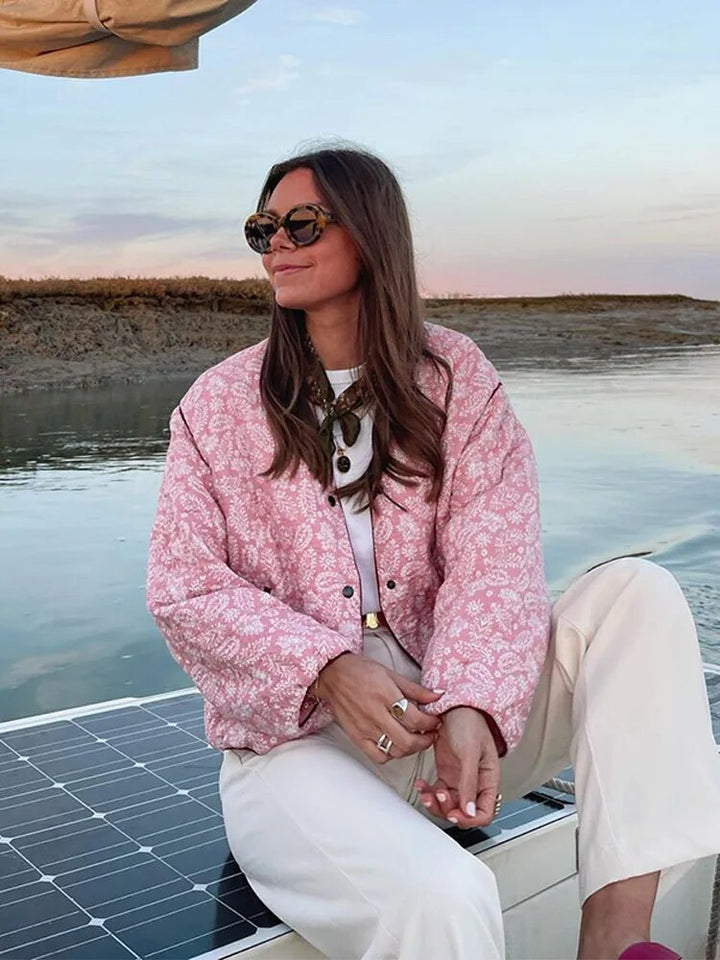 Woman wearing pink floral quilted jacket, seated on boat outdoors | Grace Aura