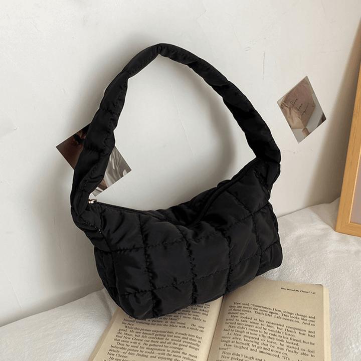 Black quilted puffer shoulder bag displayed flat on open book | Grace Aura
