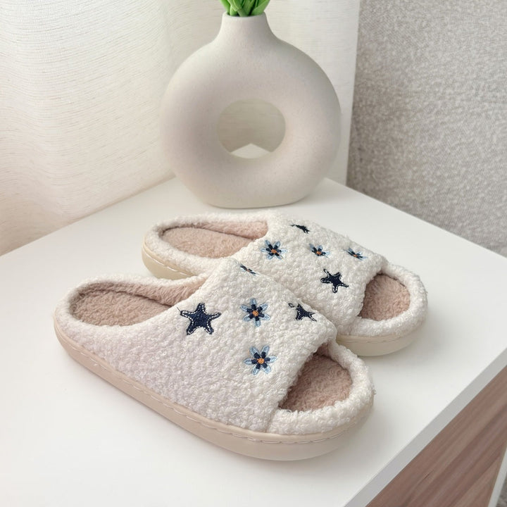 Cream fleece slippers with embroidered stars and flowers, displayed on shelf | Grace Aura