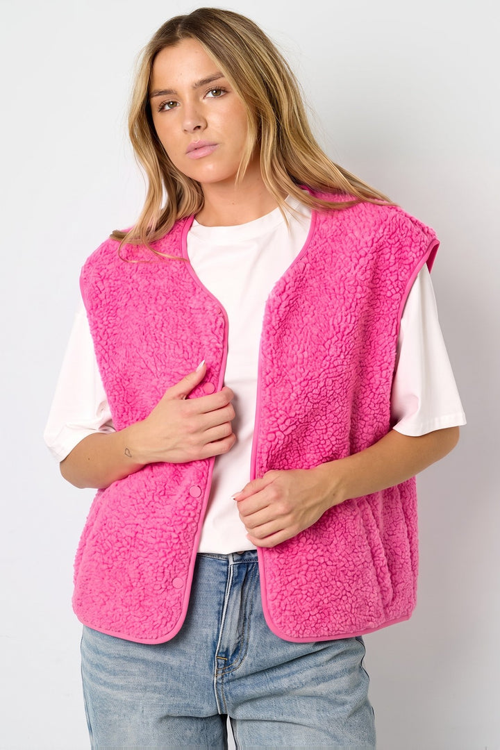 Woman wearing a pink hip-length teddy fleece vest open over a white T-shirt and jeans | Grace Aura