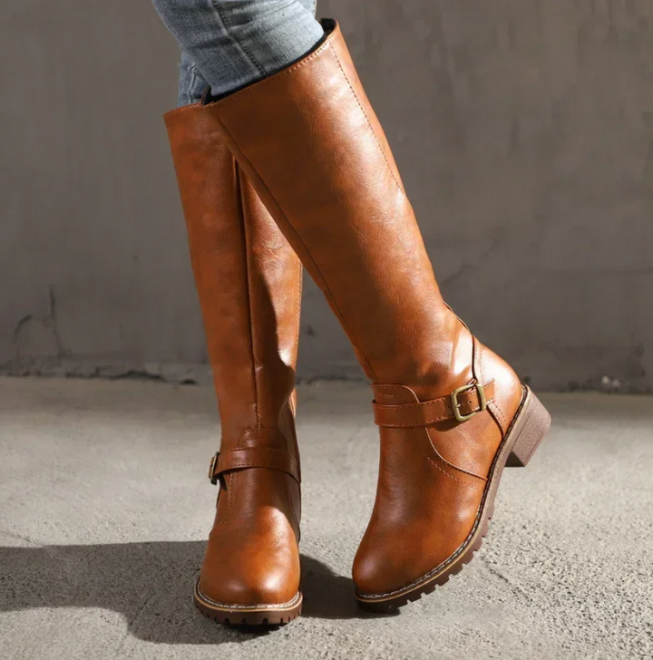 Worn brown leather knee-high boots with buckle strap detail, side view | Grace Aura