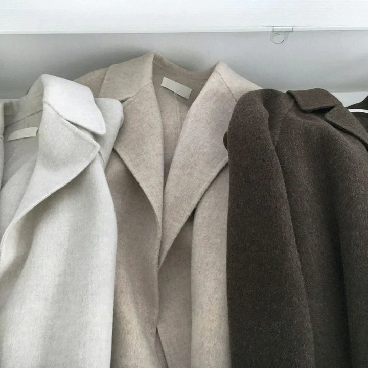 Three wool coats in white, beige, and brown hanging on rack | Grace Aura