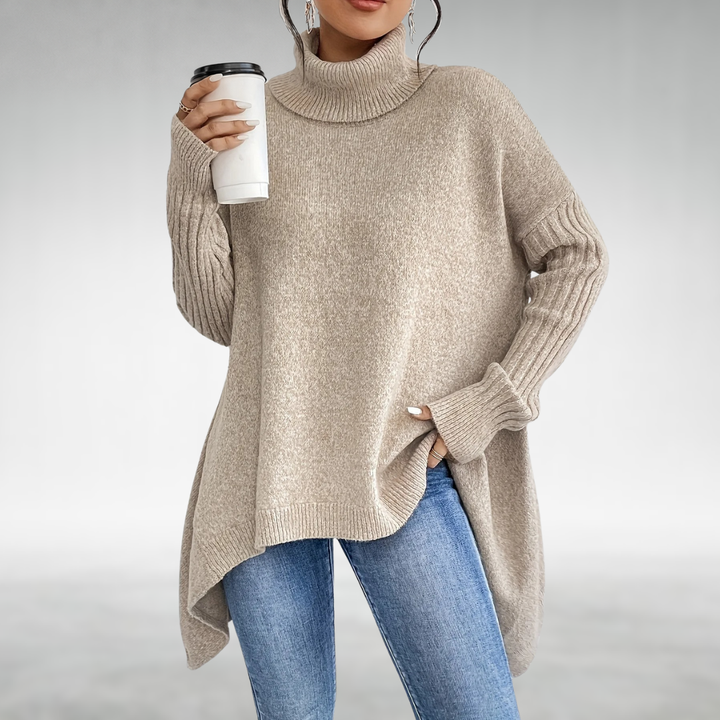 A woman wears a beige oversized turtleneck sweater while holding a coffee cup, paired with blue jeans