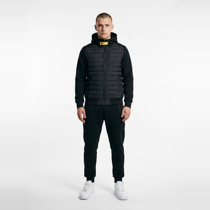 Man wearing black quilted hooded jacket with matching joggers and white sneakers | Grace Aura