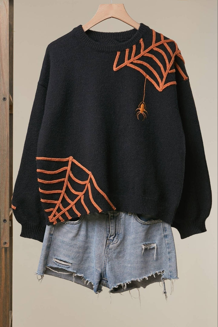 Black jumper with orange spider web embroidery on a hanger, front view