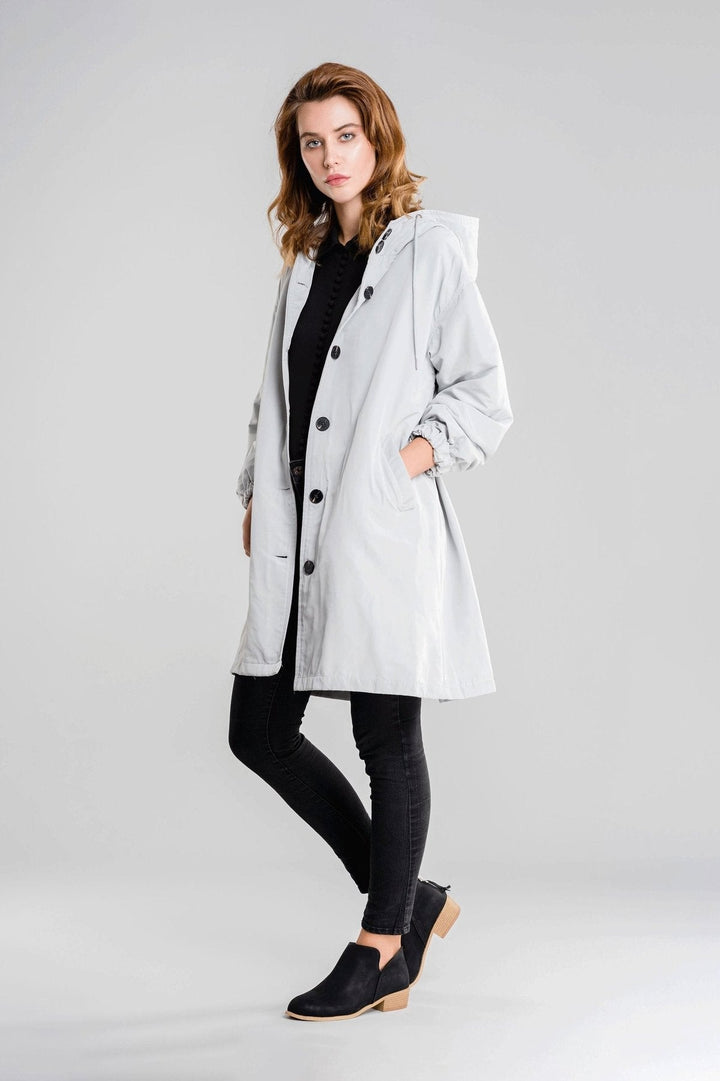 Ice grey hooded raincoat, buttoned, over a black top with one hand in the pocket