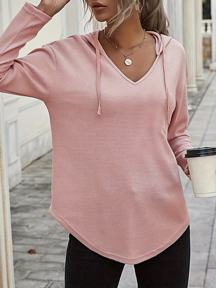 Woman wearing a dusty pink V-neck hoodie, holding a coffee cup with one hand in her hair | Grace Aura