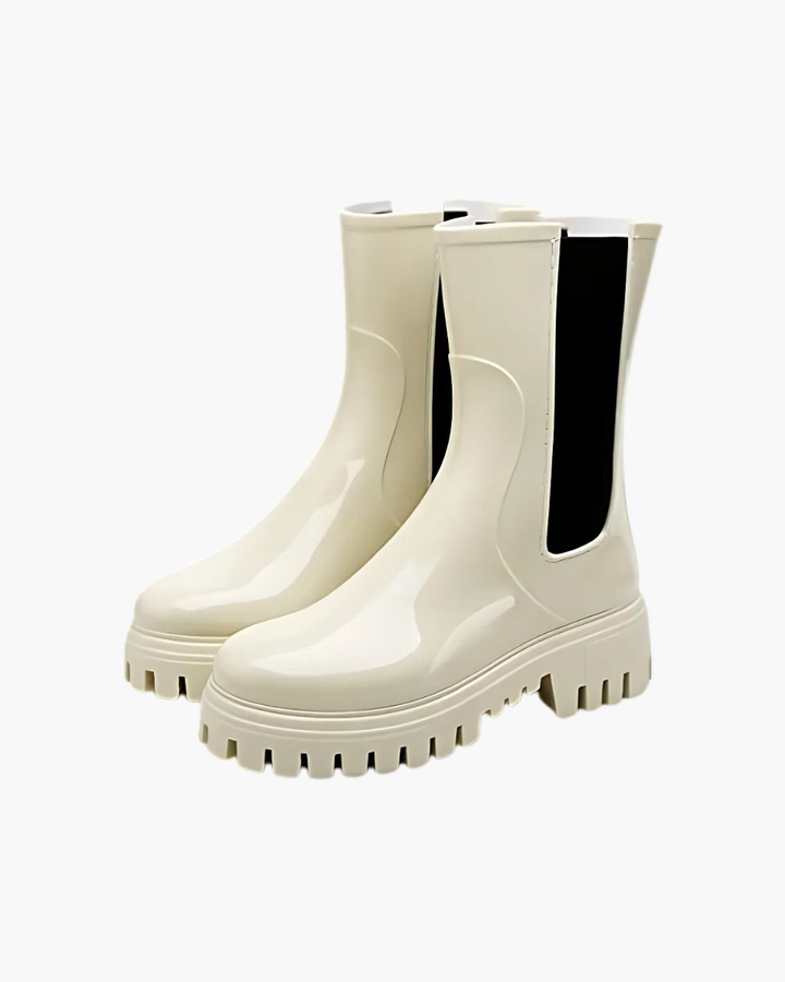 A pair of glossy cream rubber Chelsea boots with black elastic side panels and chunky lug soles, shown in a three quarter view on a plain white background.