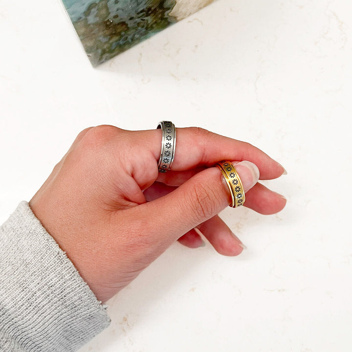 Silver and gold daisy-engraved spinner rings worn on hand fingers together | Grace Aura