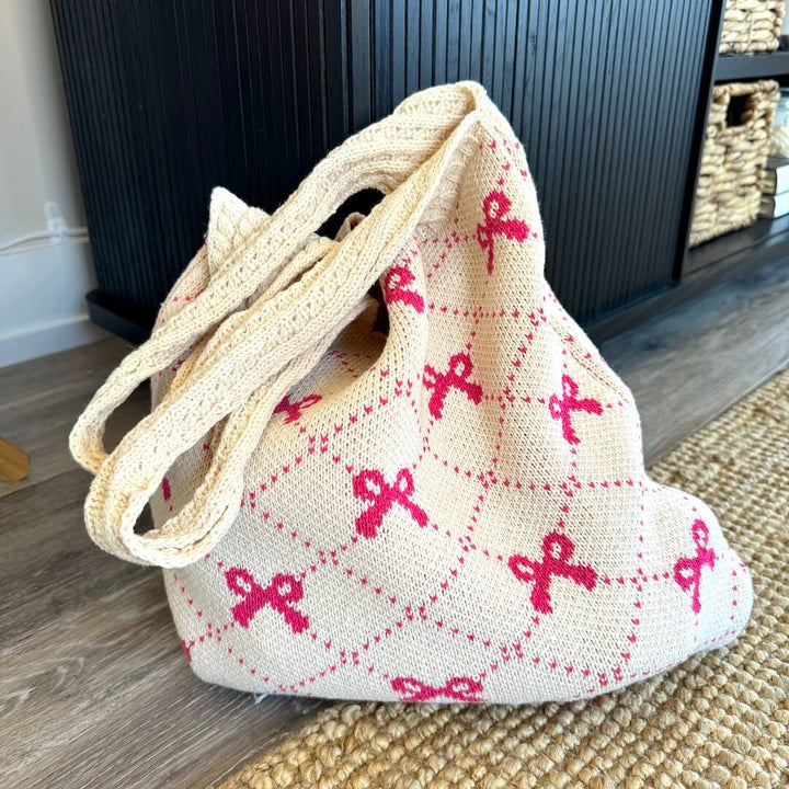 Beige crochet tote bag with pink bow print, resting on floor | Grace Aura