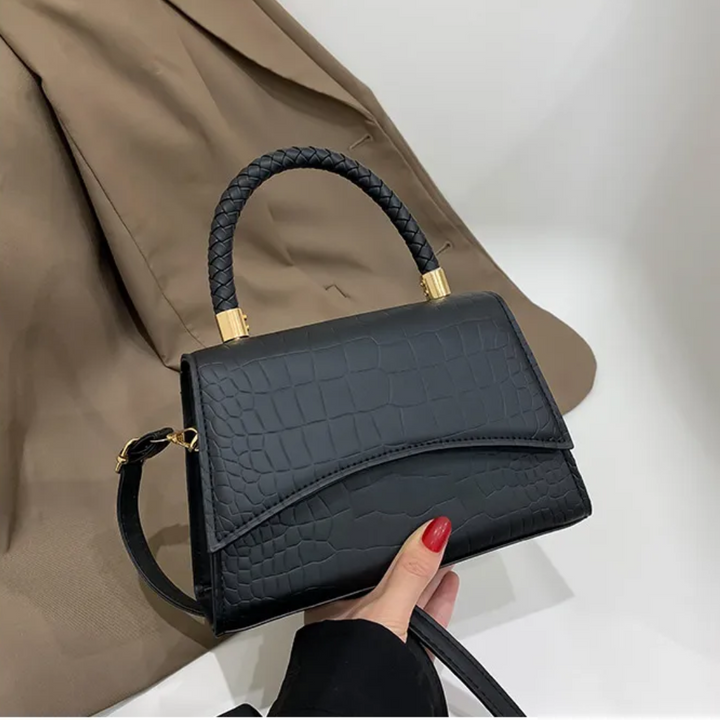 Black crocodile-embossed handbag with braided top handle, held by hand | Grace Aura