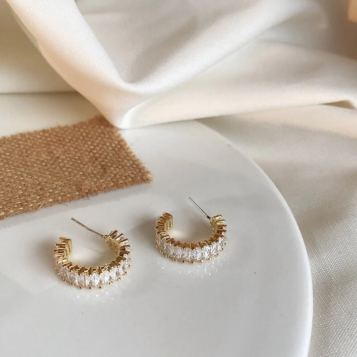 Gold C-hoop earrings with clear crystals, displayed flat on white surface | Grace Aura