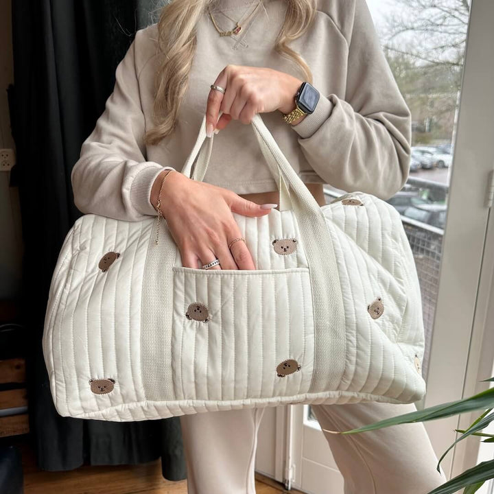 Cream quilted duffle bag with brown bear print, held by woman | Grace Aura