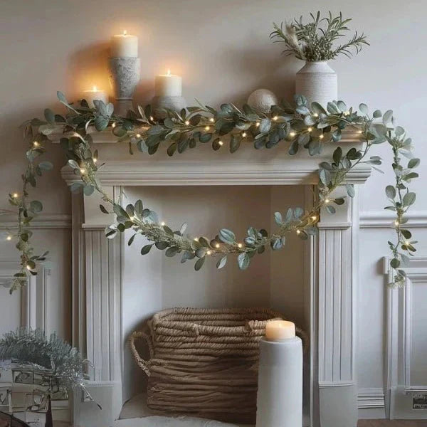 Green eucalyptus garland with warm lights draped on white fireplace mantel | Grace Aura
