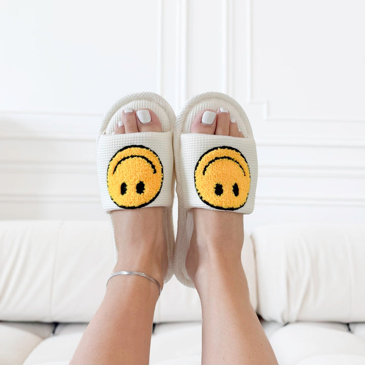 White terry cloth slides with yellow smiley face patch, worn by feet | Grace Aura
