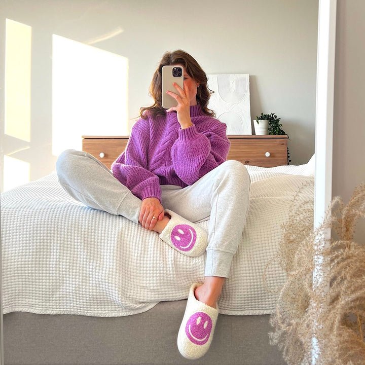 White fuzzy slippers with pink smiley faces worn by seated woman | Grace Aura