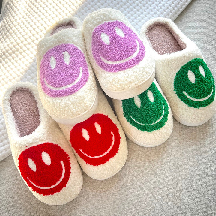 Fuzzy cream slipper pairs with purple, red, and green smiley faces | Grace Aura