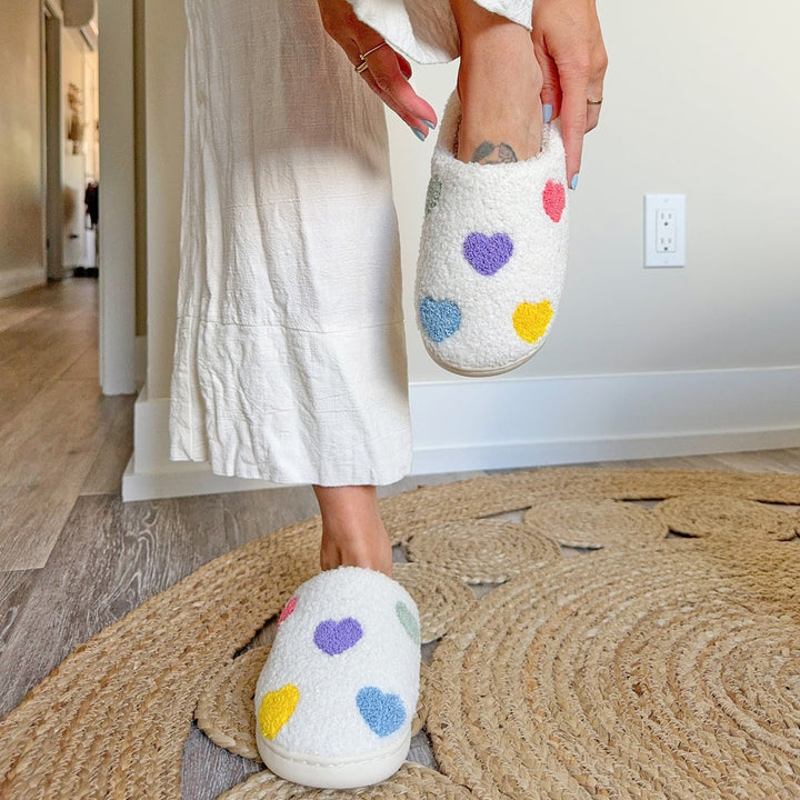 White plush slipper with colorful heart pattern, worn on person&