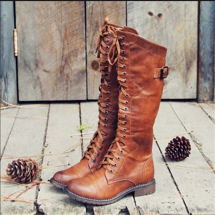 Brown leather knee-high lace-up boots standing on wooden plank floor outdoors | Grace Aura