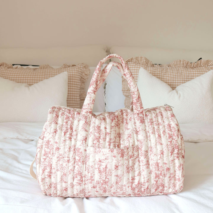 Quilted pink floral duffle bag with handles displayed on bed | Grace Aura
