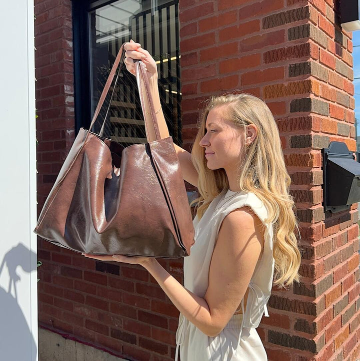 Woman holding brown faux leather tote bag outdoors near brick wall | Grace Aura