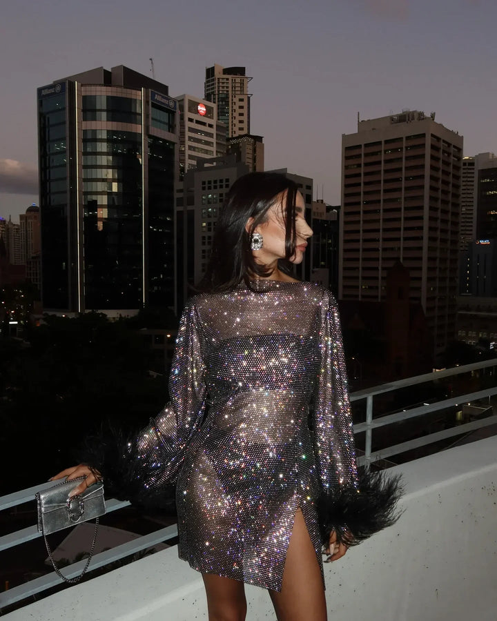 Woman wearing sparkly sequin long-sleeve mini dress with feather cuffs outdoors | Grace Aura