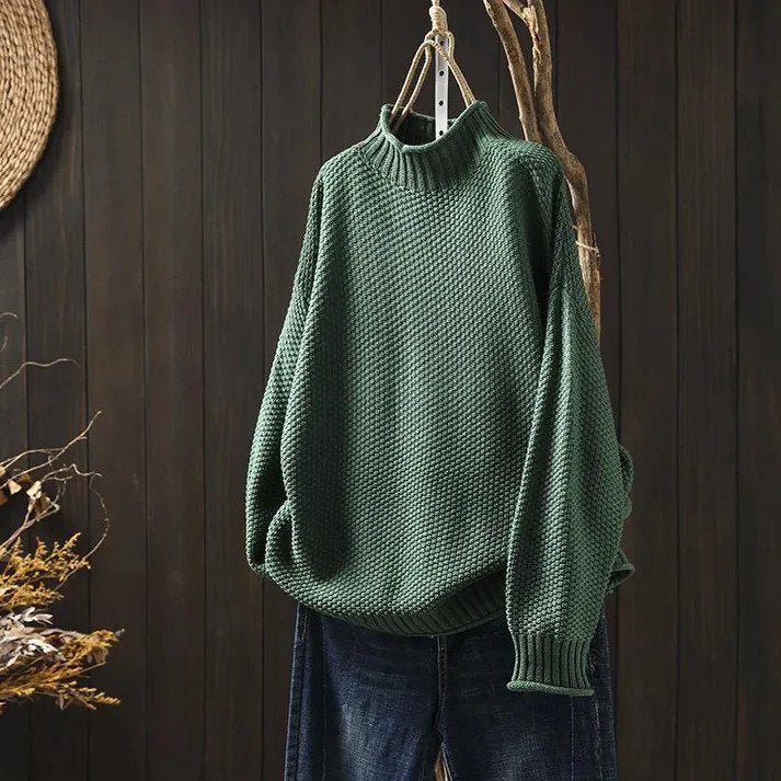 Green knitted turtleneck sweater hanging on wooden hanger against dark wall | Grace Aura