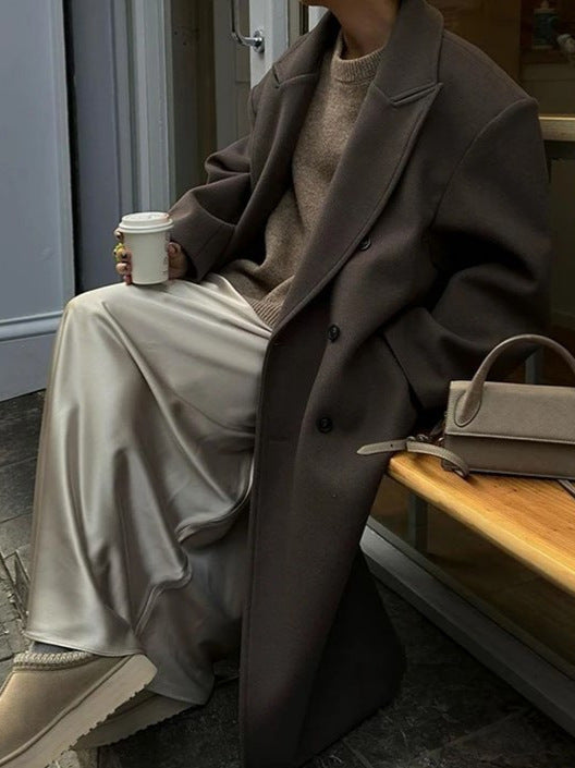 Brown oversized wool coat worn by seated person with beige trousers | Grace Aura