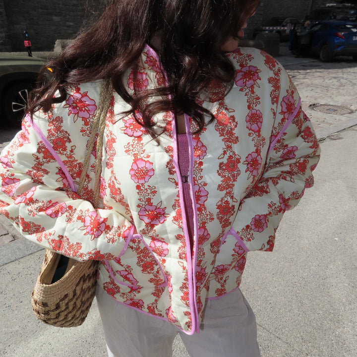 Woman wearing cream floral quilted jacket with pink trim, carrying woven bag | Grace Aura