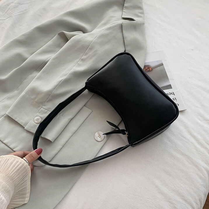 Black PU leather baguette bag held by hand, sage garment background | Grace Aura