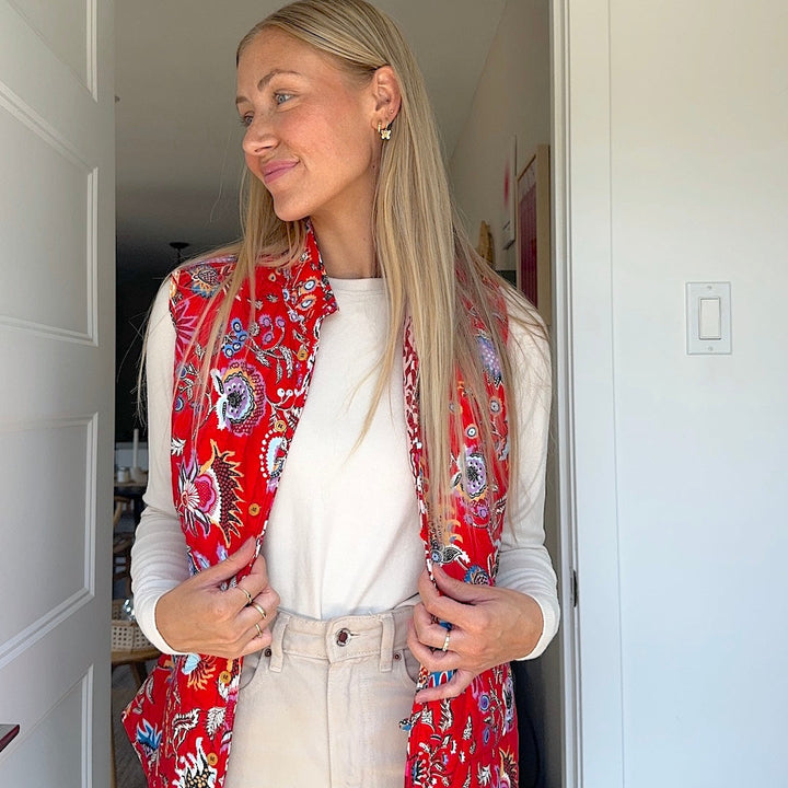 Woman wearing red floral quilted vest over white shirt indoors | Grace Aura