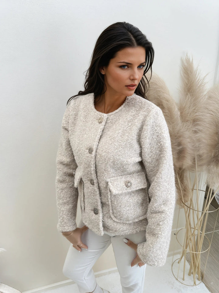 Woman wearing beige boucle button-up jacket with pocket, white pants, indoor setting | Grace Aura