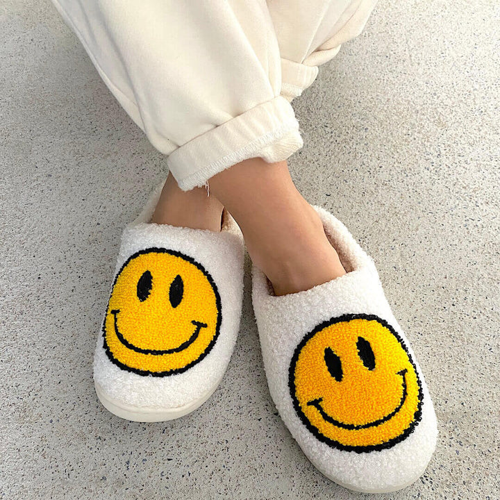 White fuzzy slippers with yellow smiley face patches, worn by person | Grace Aura